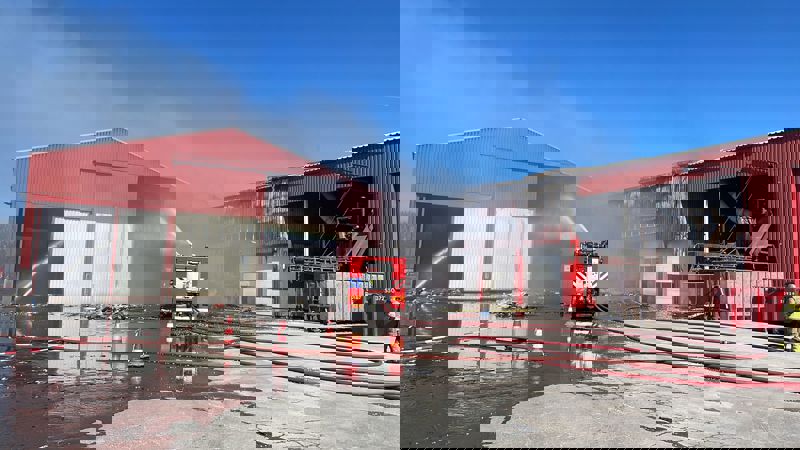 Brandweermensen blussen de loods waar nu minder rook te zien is