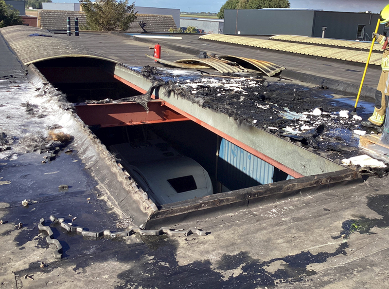 Beeld van het dak waar de lichtkoepel voor een groot deel is weggebrand. Een brandweerman checkt het dak op brandvorming. 