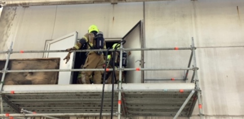 Brandweerman op een soort steiger aan de buitenkant van de fabriek 