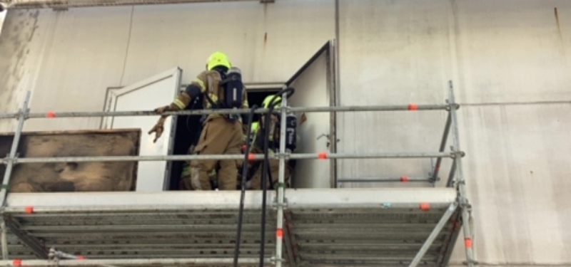 Brandweerman op een soort steiger aan de buitenkant van de fabriek 