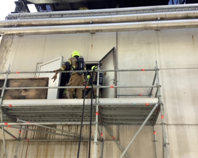 Brandweerman op een soort steiger aan de buitenkant van de fabriek 